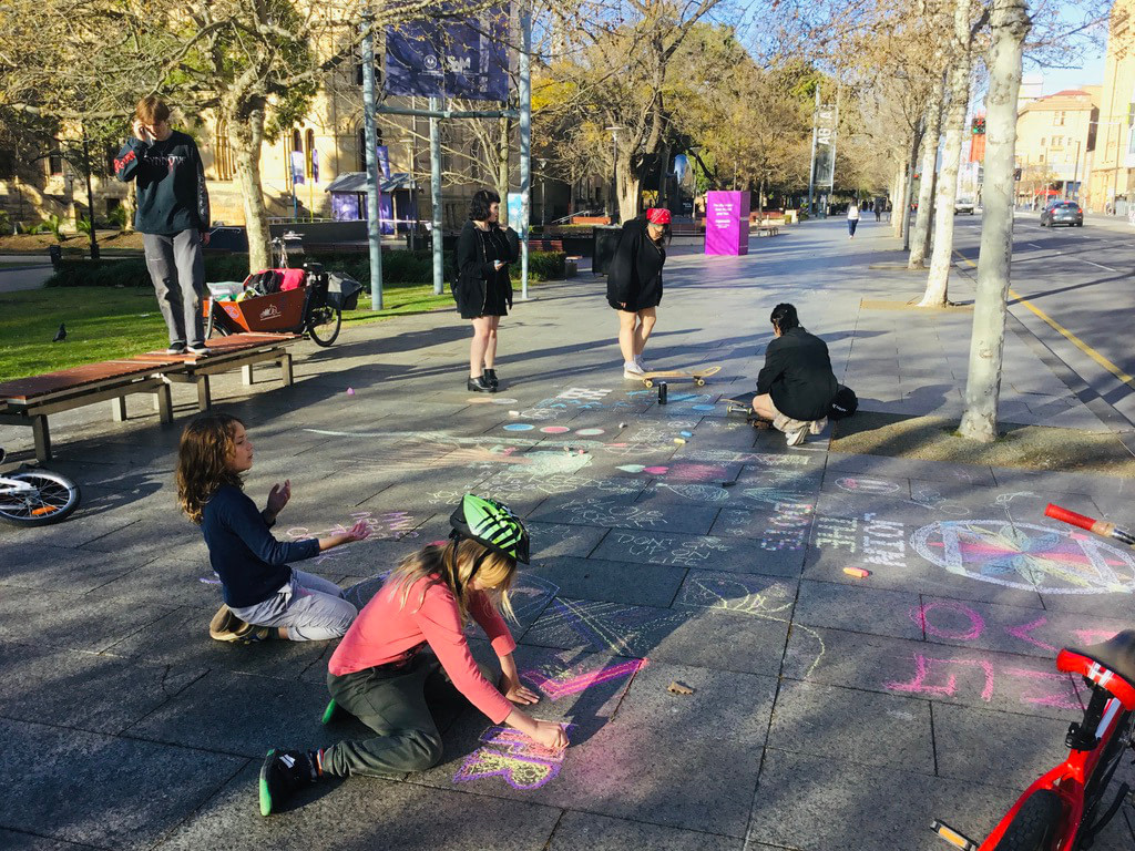 children and teenagers chalking dotzero, pictures and messages of hope on city pavement
