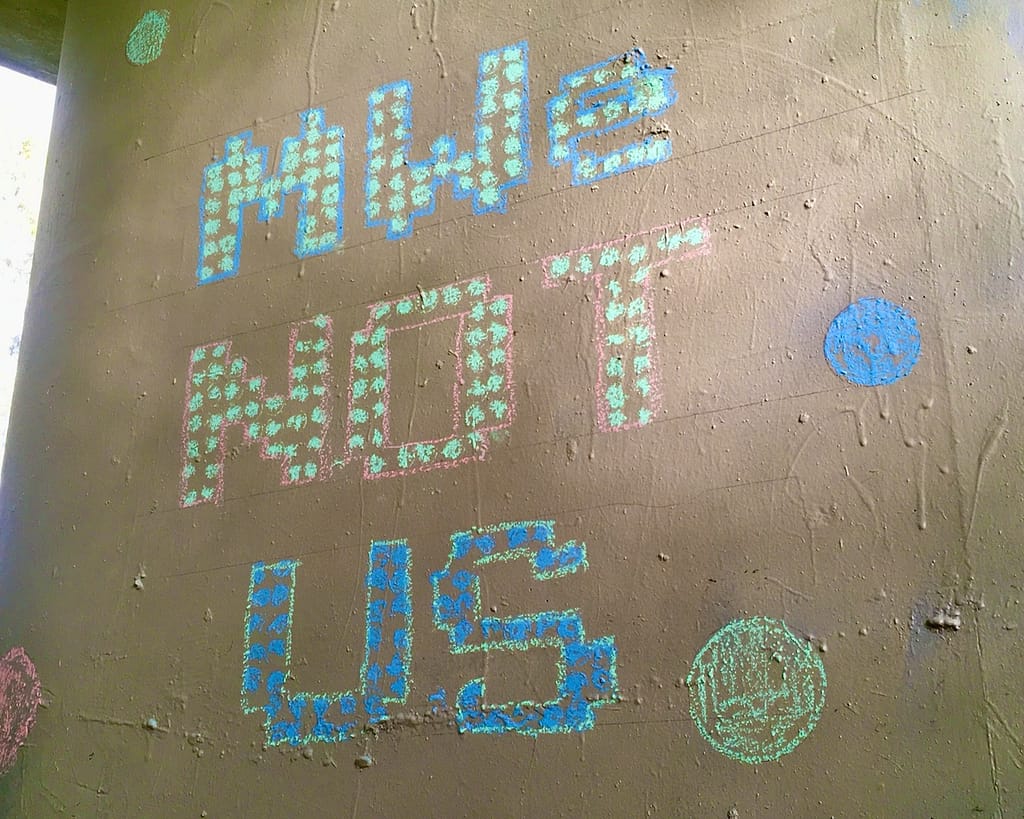 Example of long game meme: 'MWe not Us' in chalk on pillar