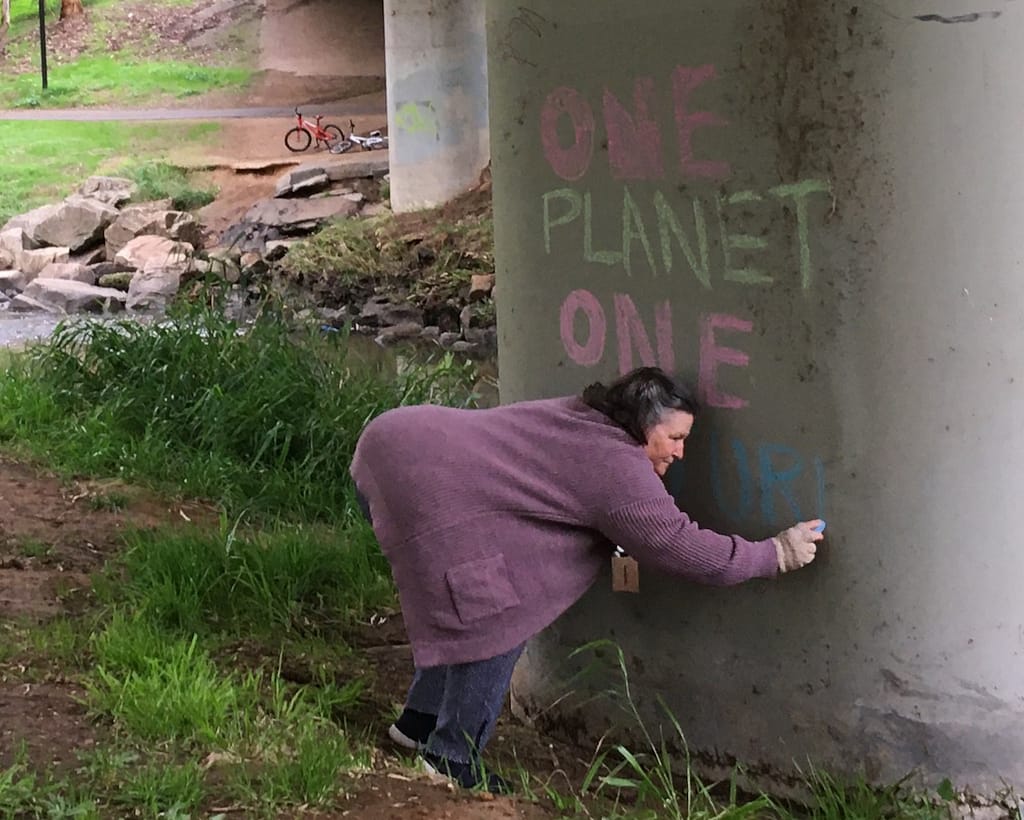 Woman chalking 'One Planet, One Future' on pillar