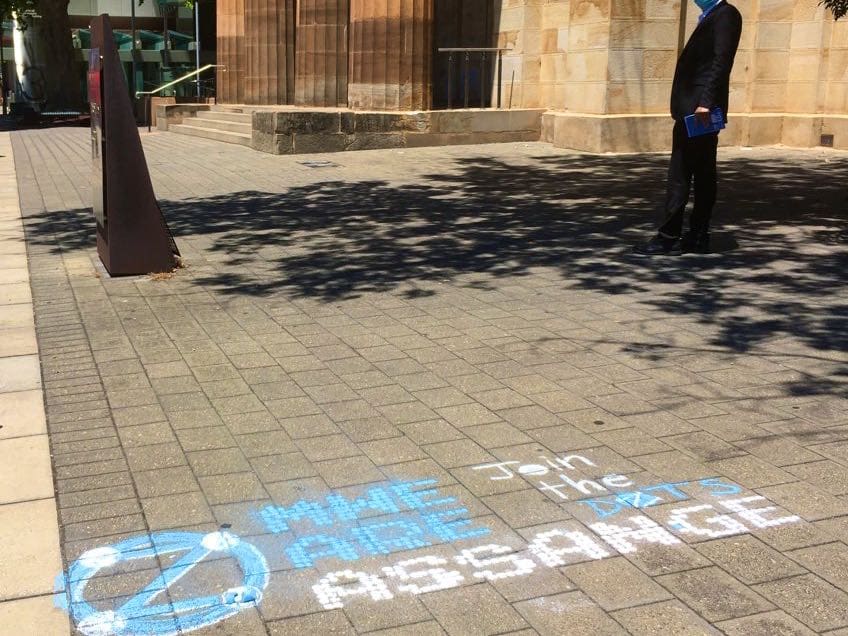 Example 'MWe Are Assange' in chalk, at courthouse